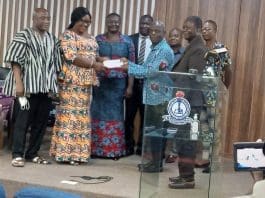 Ms Phillipa Lassen, the President of GNAT, presenting the cash to Mr Raphael Kwashie, Principal of St Francis Teacher Training College on behalf of other beneficiaries. At the background are Principals and their representatives and Mr Thomas T. Musah, the General Secretary of GNAT (in Fugu).