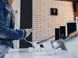 Young Attractive Girl In Electronics Store Stands At Desk And Te